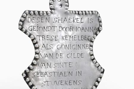 Schakelfragment van een sireschakel van de gilde van Sint-Sebastiaan te Stuivenskerke  met op de voorzijde een opschrift binnen een parelrand