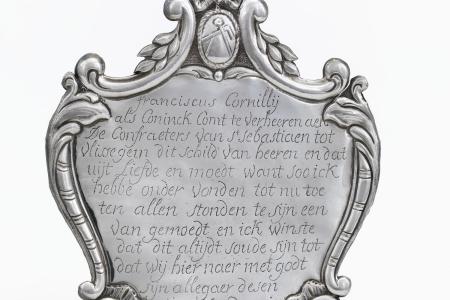 Sireteken voor Franciscus Cornillij vanwege de gilde van Sint-Sebastiaan te Vlissegem  met op de voorzijde een opschrift binnen een rocaillevormige omlijsting. Bovenaan een medaillon met passer en winkelhaak onder een strik  onderaan een Grieks kruis