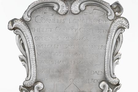 Sireteken voor Cornelis Longerspeye vanwege de gilde van Sint-Sebastiaan te Oostkerke  met op de voorzijde een opschrift geflankeerd door gereedschap binnen een rocaille vormige omlijsting . Bovenaan een ophanggat