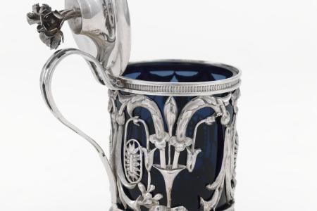 Mosterdpot van zilver en blauw glas   rond zoutvat met pootjes met handvat  deksel versierd met ajourwerk van rozen rondom versierd met bladranken en florale motieven